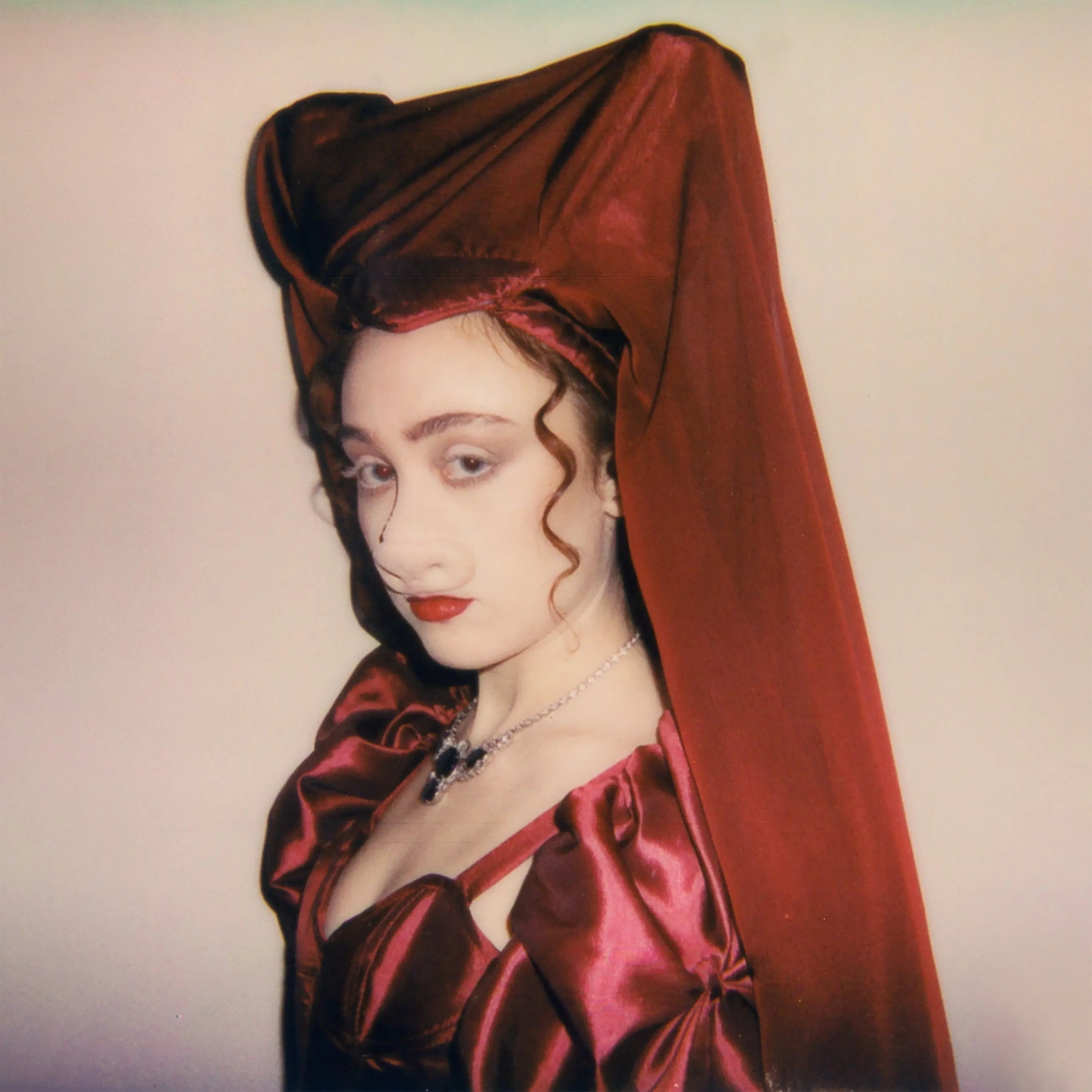 Una mujer con un tocado y vestido rojo, con maquillaje dramático y un collar.