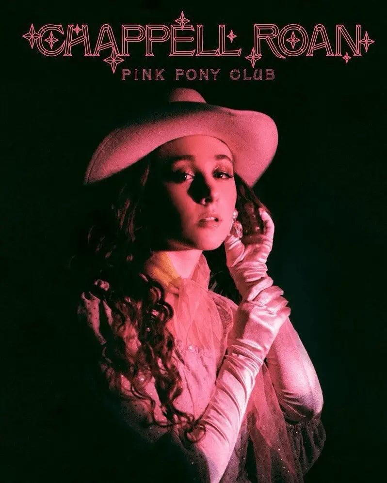 Una mujer con sombrero de vaquero rosa y guantes posa bajo una luz rosa.