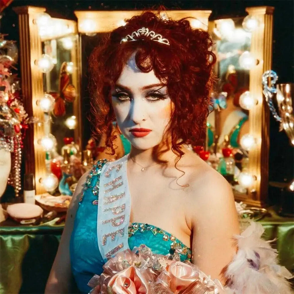 Una mujer con cabello rojo rizado, tiara y banda de "Miss Chappell" sostiene un ramo de rosas.