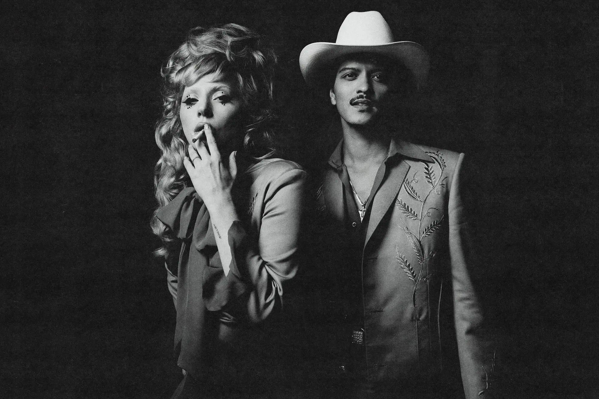 Lady Gaga y Bruno Mars posan en blanco y negro, ella fumando y él con sombrero.