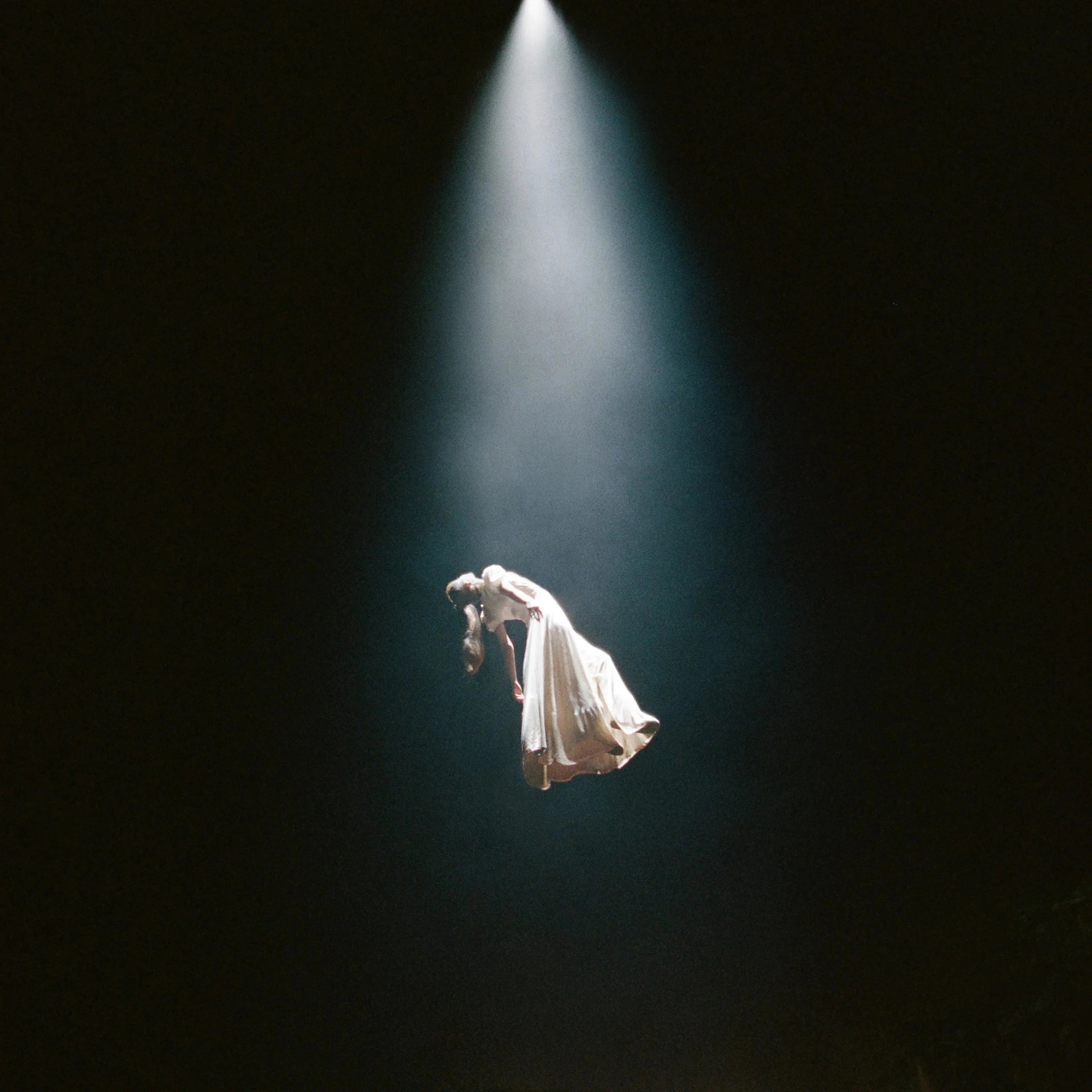 A woman in a white dress floats in a spotlight against a dark background.