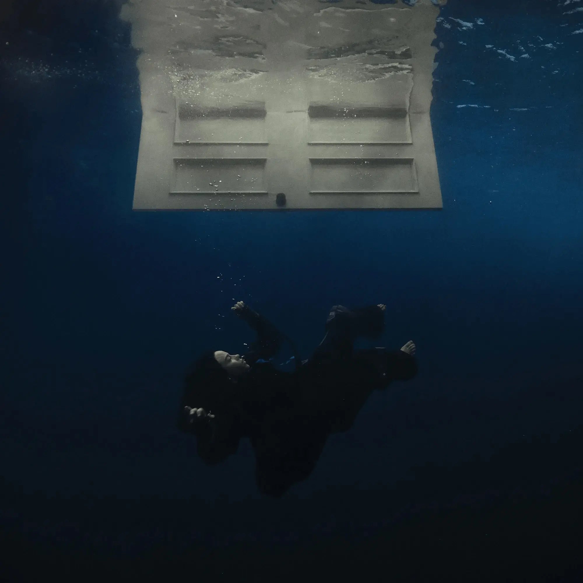 Una persona flota bajo el agua, mirando una puerta blanca flotando sobre ella.