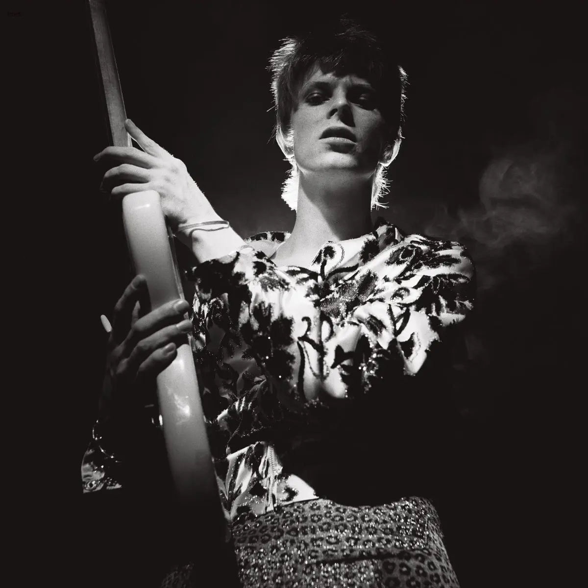 David Bowie sostiene una guitarra, con una camisa estampada y pantalones de leopardo.