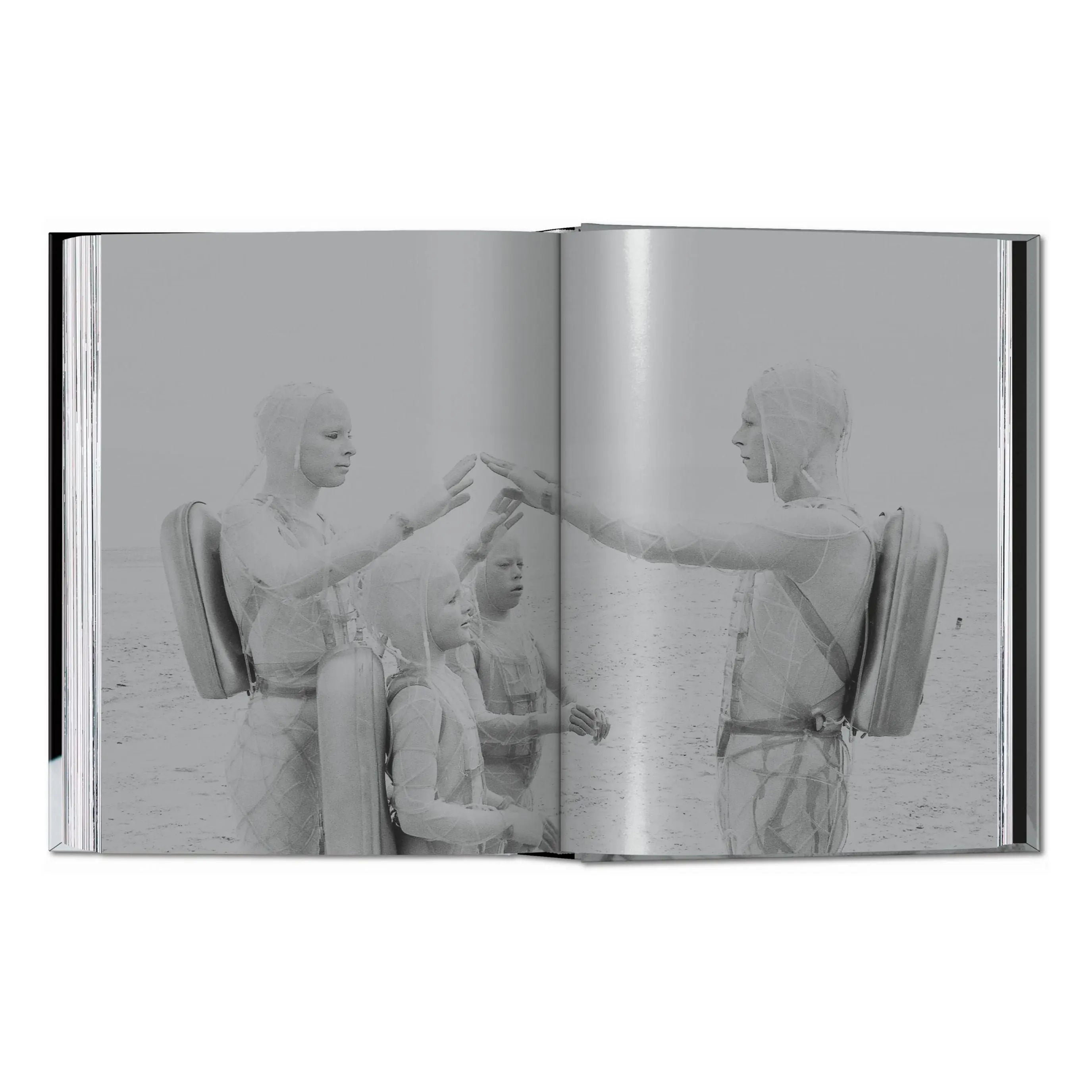 An open book displays a black and white image of four figures in futuristic suits on a sandy landscape.