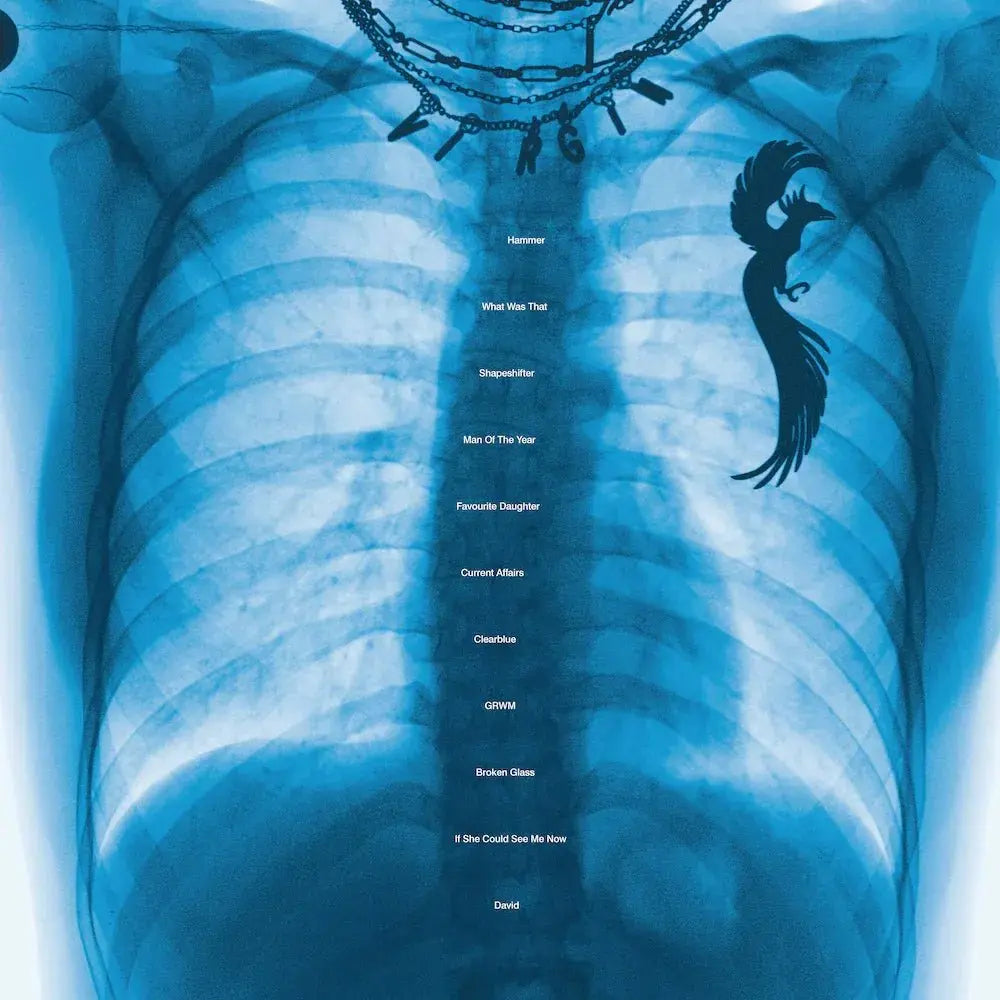 Una radiografía azul de un torso con una cadena que forma "VIRGIN" y una lista de canciones.