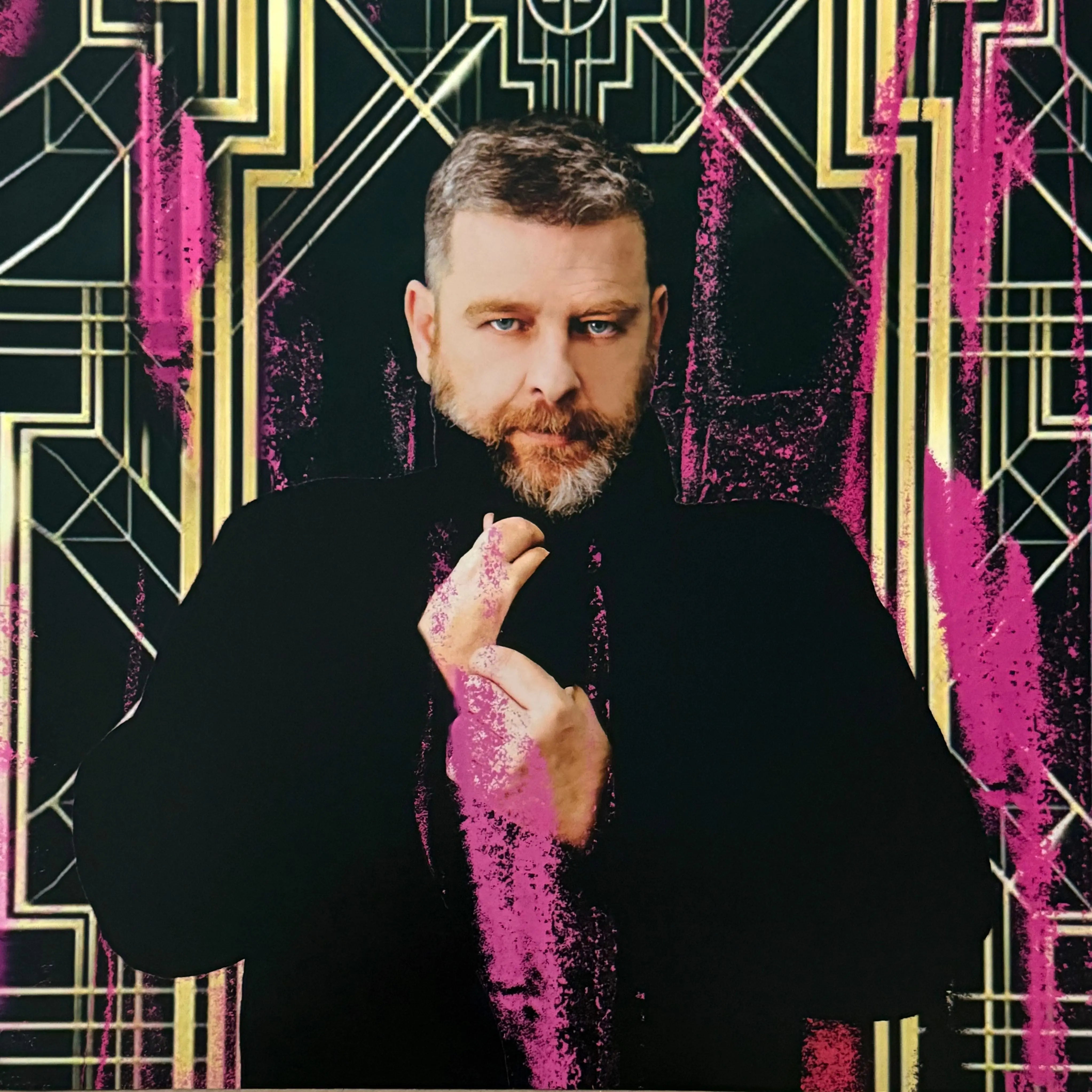 A man with a beard and blue eyes looks forward, surrounded by pink and gold art deco patterns.