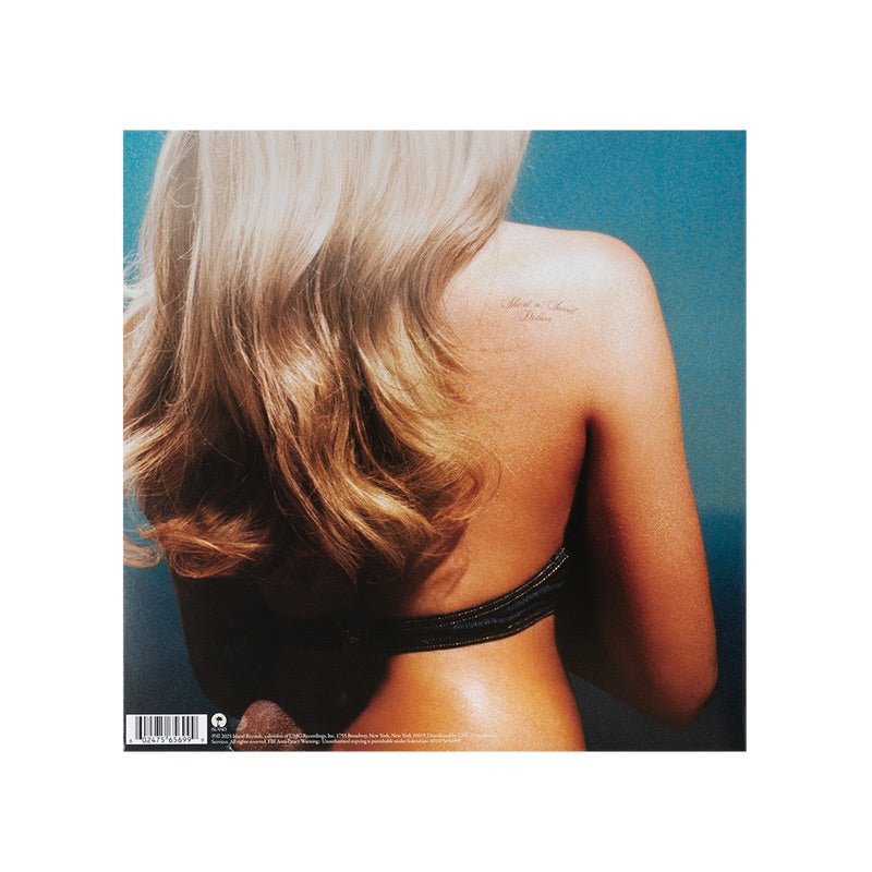 La espalda de una mujer rubia con un tatuaje "Short n' Sweet Deluxe" en el hombro.