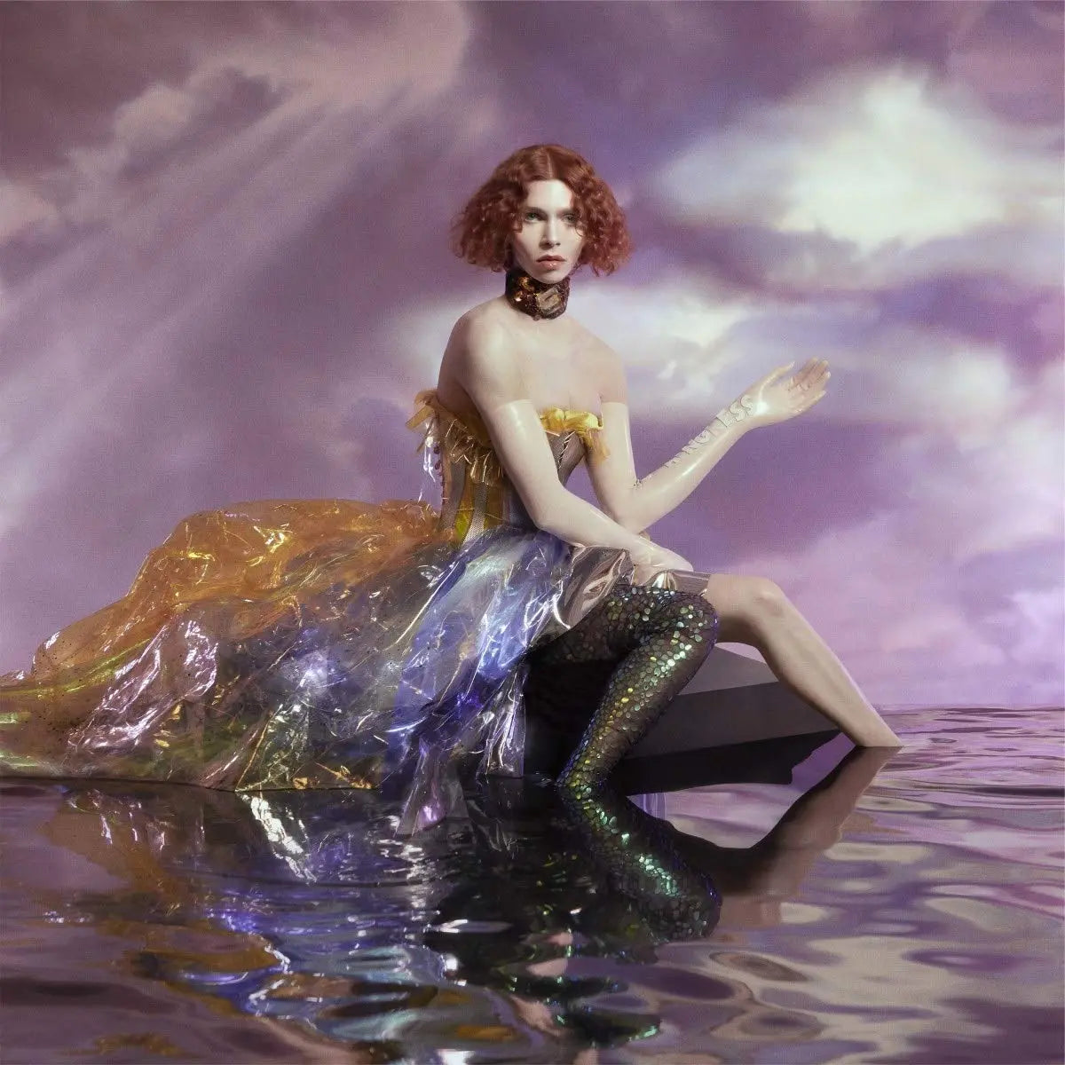 Una persona con cabello rojo rizado y un vestido iridiscente sentada en el agua.