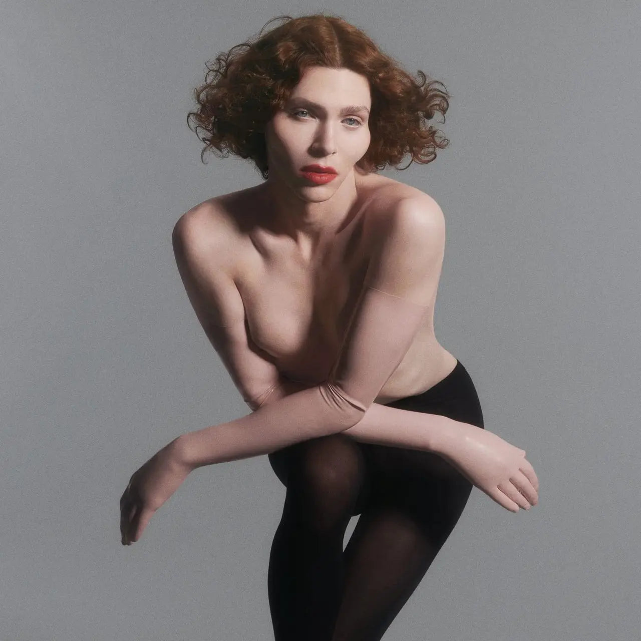 SOPHIE poses with red hair and makeup, wearing a sheer top and black tights.