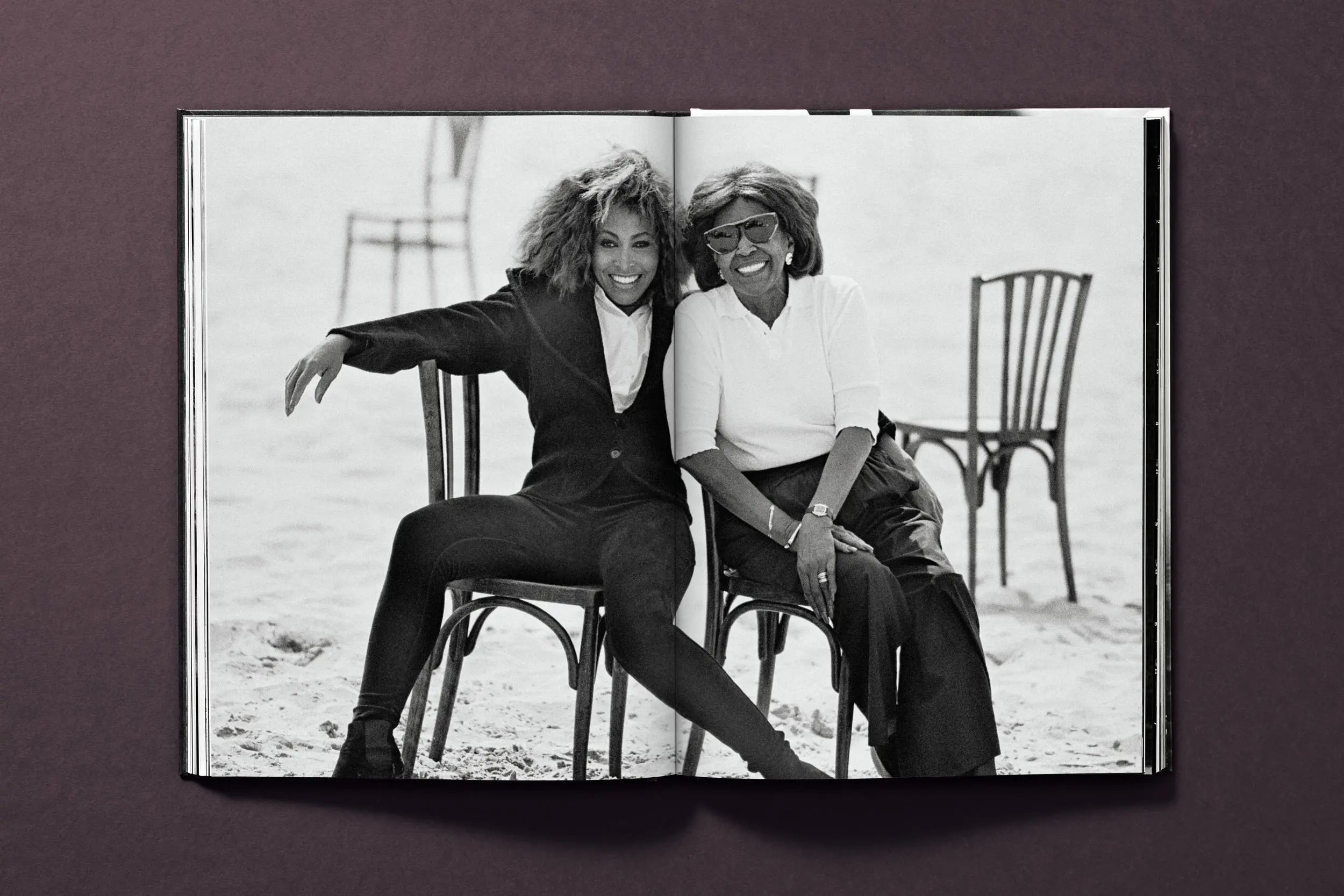 A black and white photo of Tina Turner and another woman sitting on chairs.